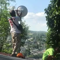A TINKIT technician aligning a dish antenna on a rooftop above the hills